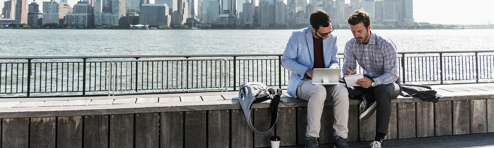 2 men working on a bench along an esplanade with a view of Manhattan