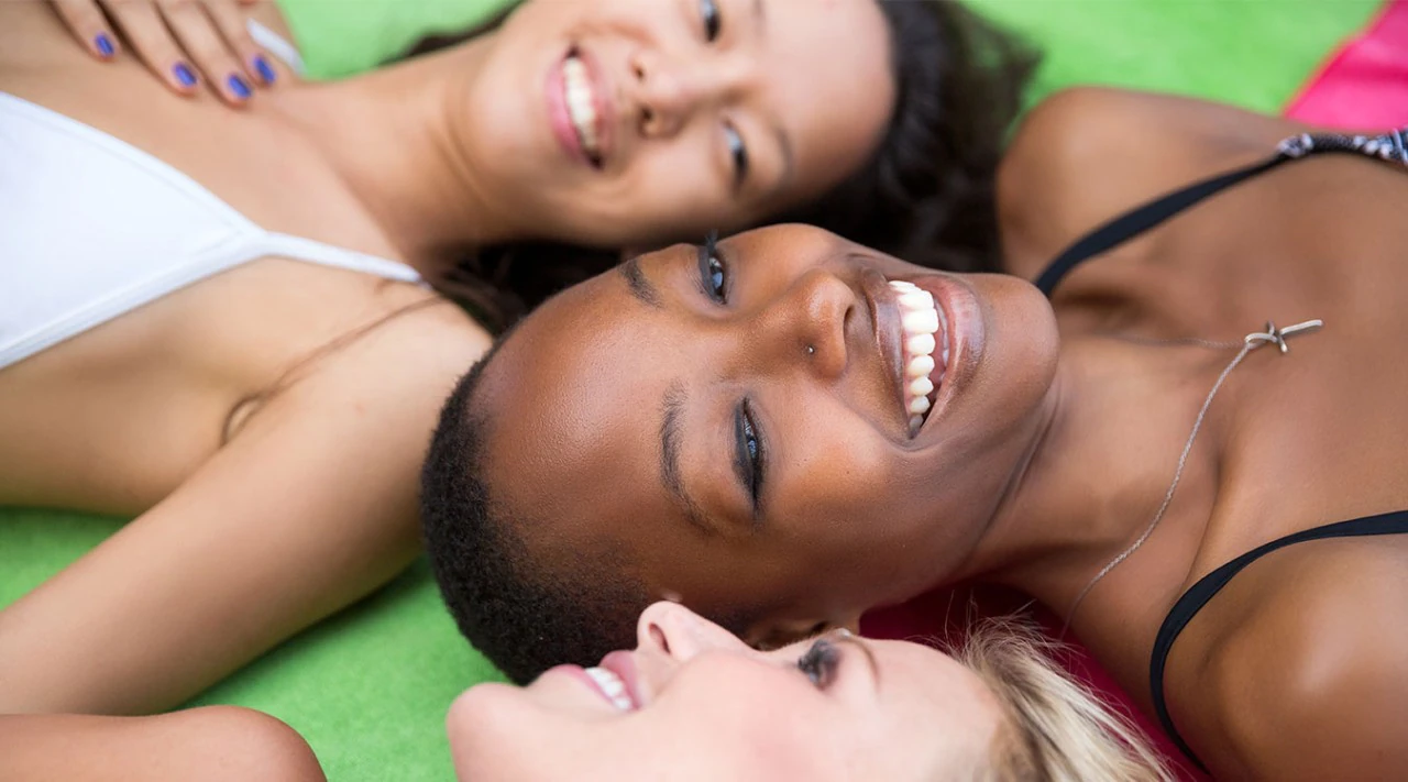 Three smiling young women sunbathing.